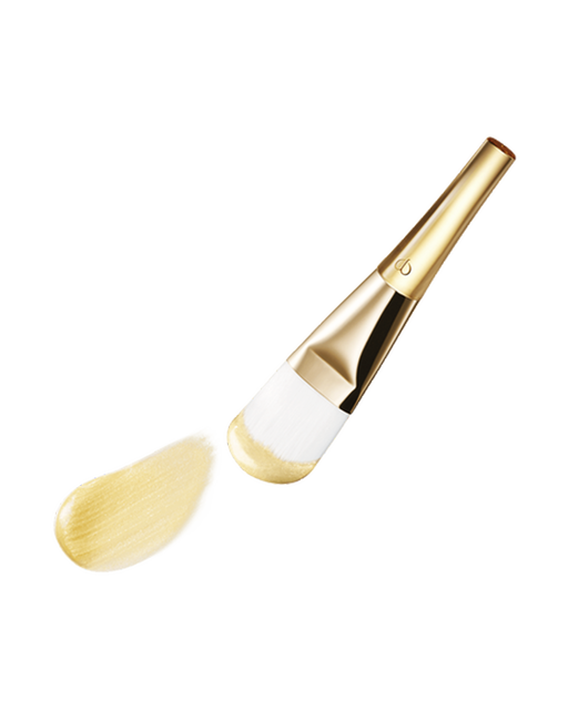 Photo of a gold-handled brush with white bristles, coated in the "PRECIOUS GOLD VITALITY MASK".