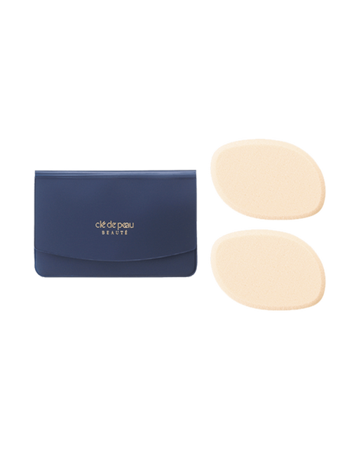 Photo of “SPONGE (FOR CREAM FOUNDATION)” showing two cream-colored oval sponges placed next to a blue-black case. The center of the case features the gold brand logo.