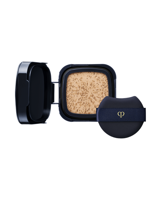 Photo of a "RADIANT CUSHION FOUNDATION DEWY (Refill)" refill case. Accompanied by a round navy puff with a gold logo. SHADE: O20