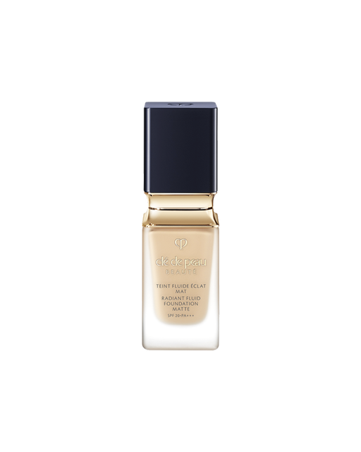 Photo of a bottle of "RADIANT FLUID FOUNDATION MATTE". The liquid foundation comes in a thick, clear glass bottle, featuring a blue-black, square-shaped cap and a gold neck accent. SHADE: O20