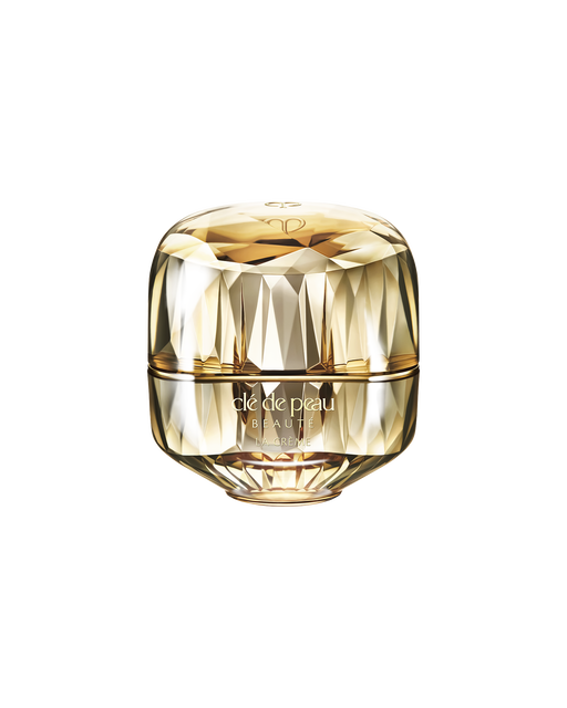 Photo of a jewel-cut, translucent gold container. The sparkling form reflects light, and the front features the brand logo and the text “LA CRÈME”.