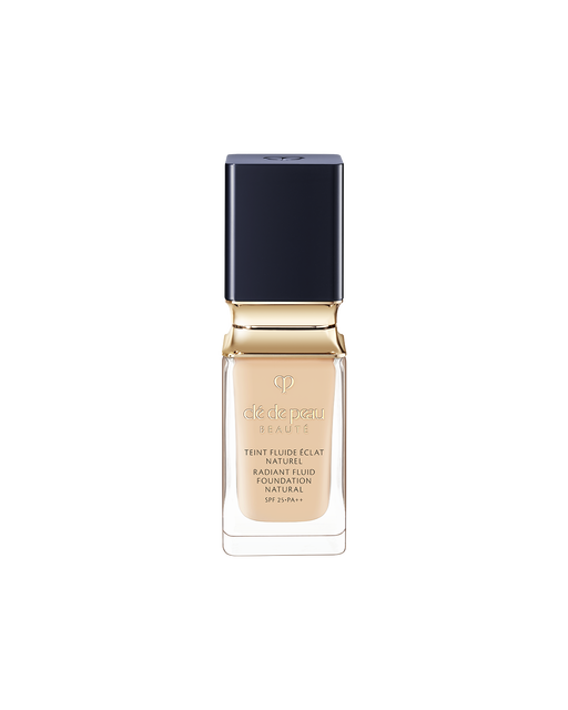 Photo of a bottle of "RADIANT FLUID FOUNDATION NATURAL". The liquid foundation comes in a thick, clear glass bottle, featuring a blue-black, square-shaped cap and a gold neck accent. SHADE: O20