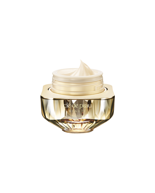 Photo of Clé de Peau Beauté’s high-performance cream “La Crème,” housed in a jewel-cut, translucent gold container. The lid is open, revealing the smooth cream inside.