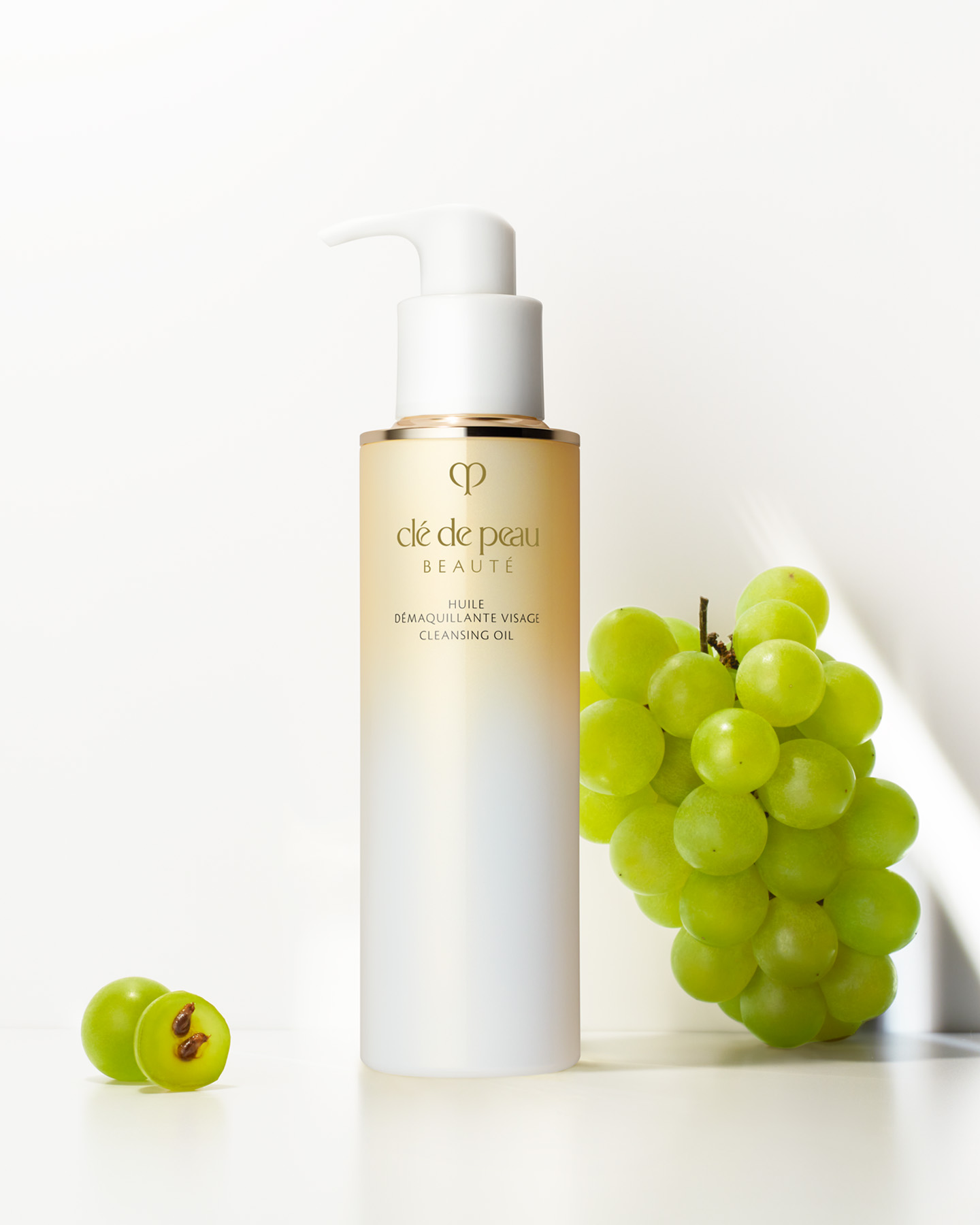 Photo of Clé de Peau Beauté CLEANSING OIL shown with a bunch of fresh grapes to emphasize the grape seed oil in the formula.