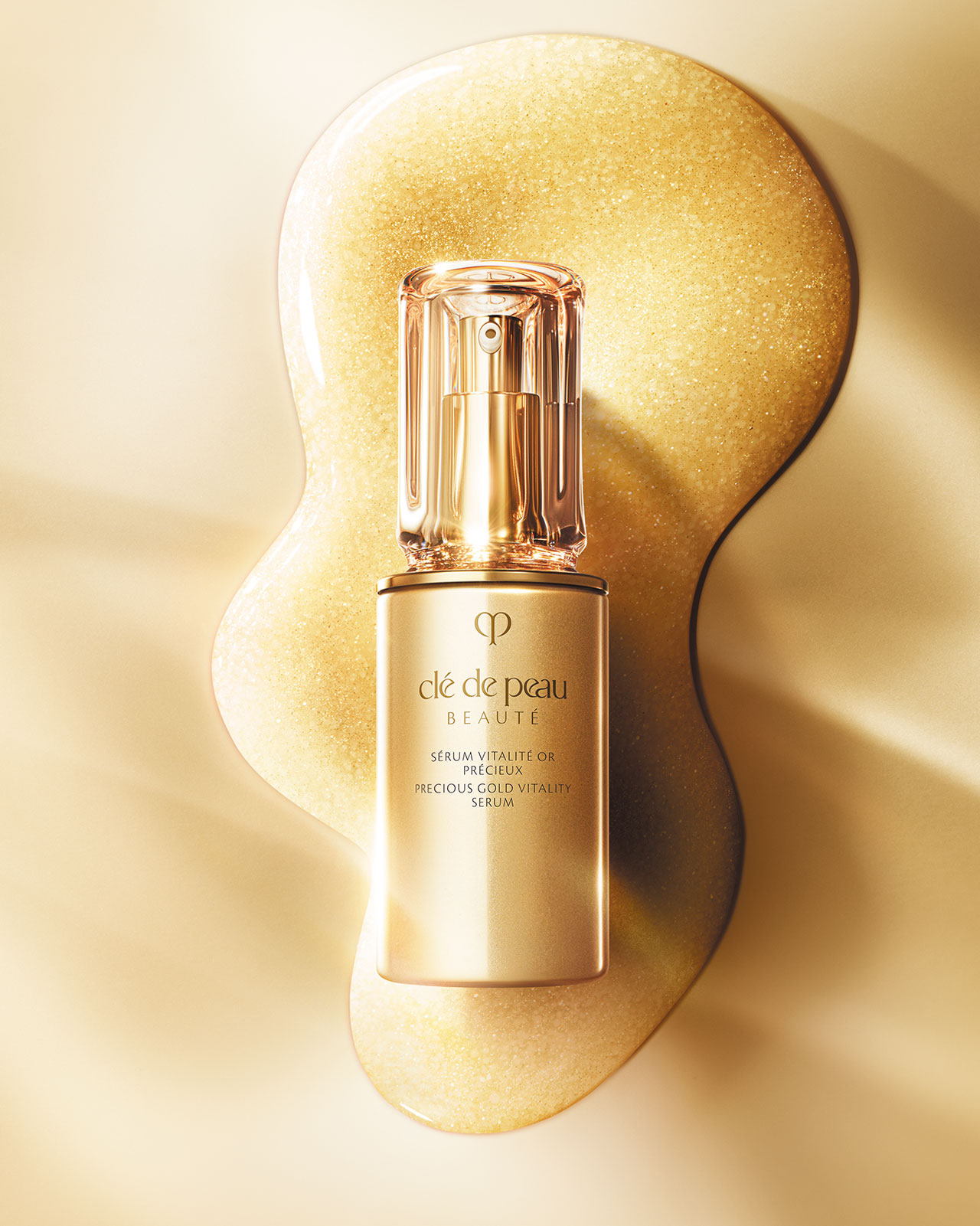 Photo of Clé de Peau Beauté's Precious Gold Vitality Serum bottle elegantly placed on a rich, shimmering swatch of the serum's 24K gold-infused texture, conveying its luxurious quality.