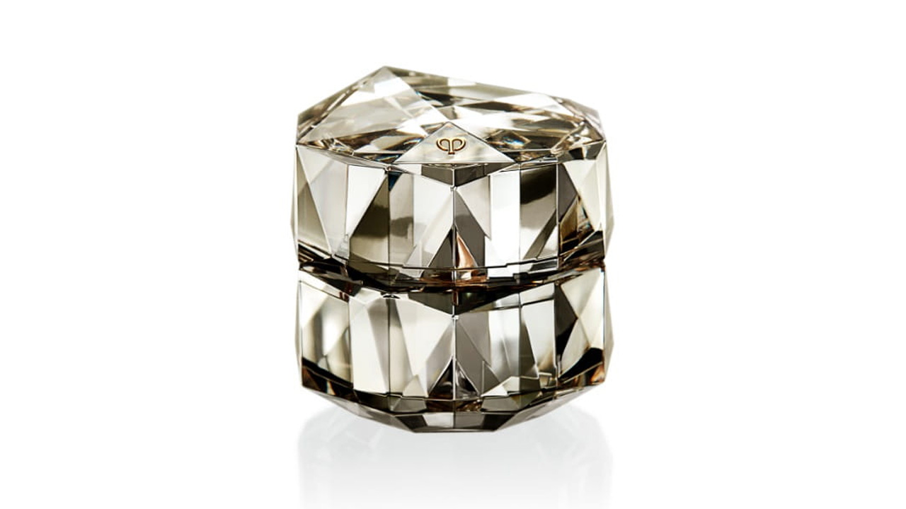 Photo of a container with diamond-like multifaceted cuts. The entire surface glows with a soft champagne gold finish, and the brand logo is displayed at the center of the lid (former packaging).