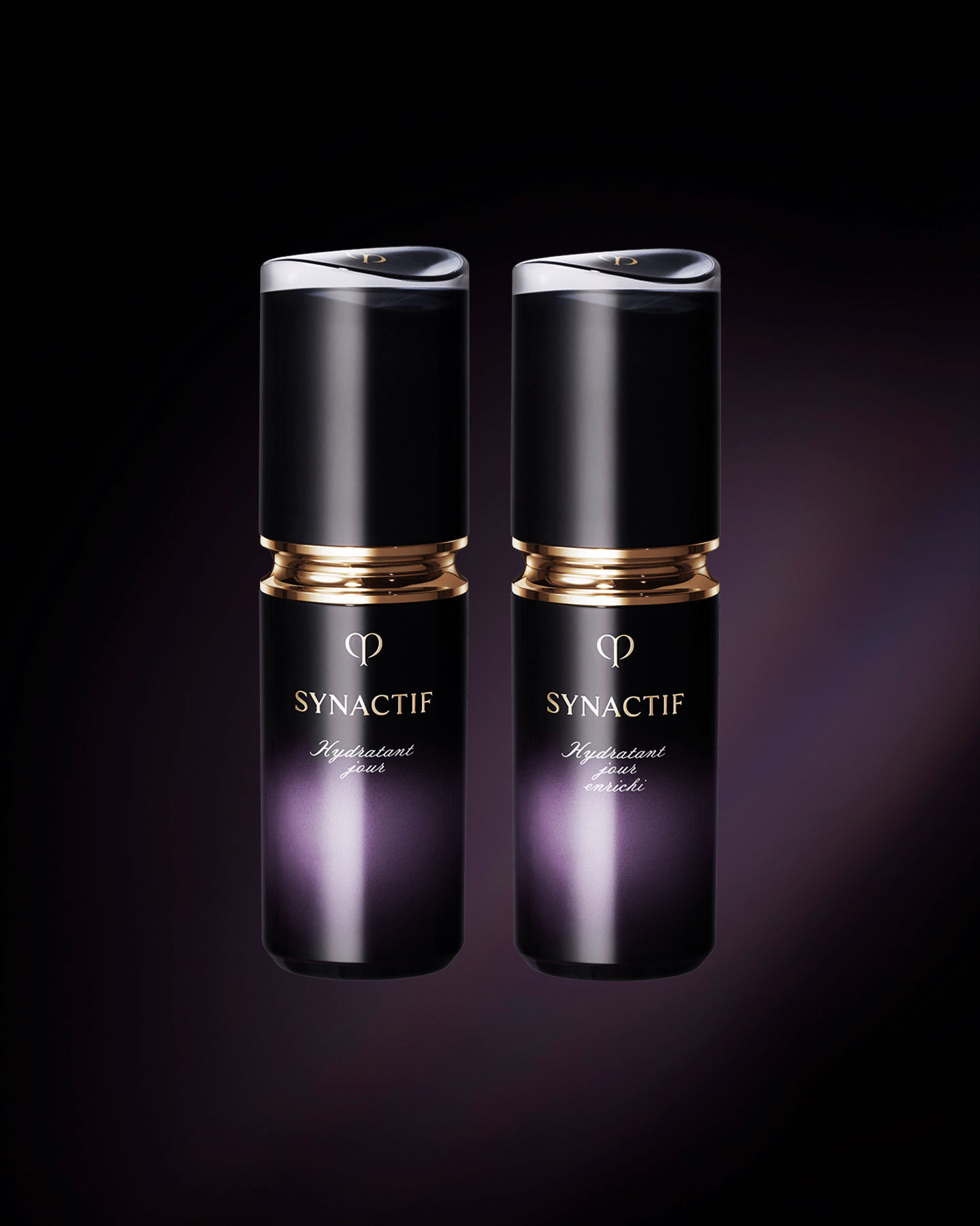 Photo of the Clé de Peau Beauté SYNACTIF DAYTIME MOISTURIZER (left) and DAYTIME MOISTURIZER ENRICHED (right). Both are housed in compact cylindrical bottles featuring a black-to-purple gradient. A gold accent is placed between the cap and body, and the 'SYNACTIF' logo is displayed on the front.