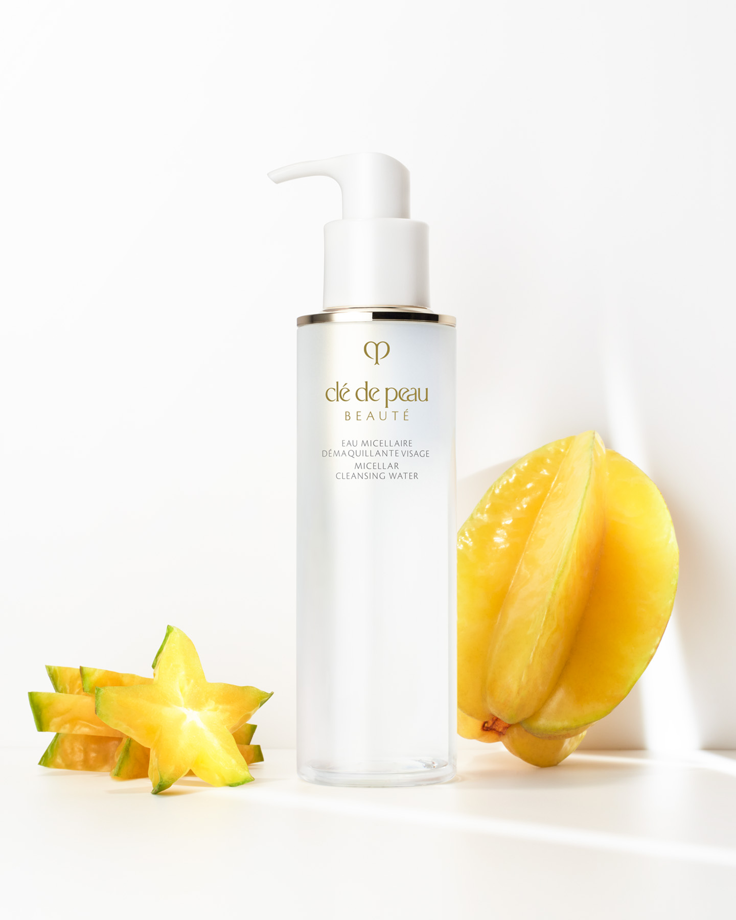 Photo of a bottle of Clé de Peau Beauté MICELLAR CLEANSING WATER placed beside a whole and sliced star fruit, highlighting the star fruit extract ingredient.