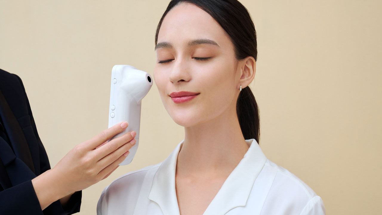 Photo of a Clé de Peau Beauté personal beauty specialist using a Handy Skin Sensor (HSS) to measure a customer’s skin.