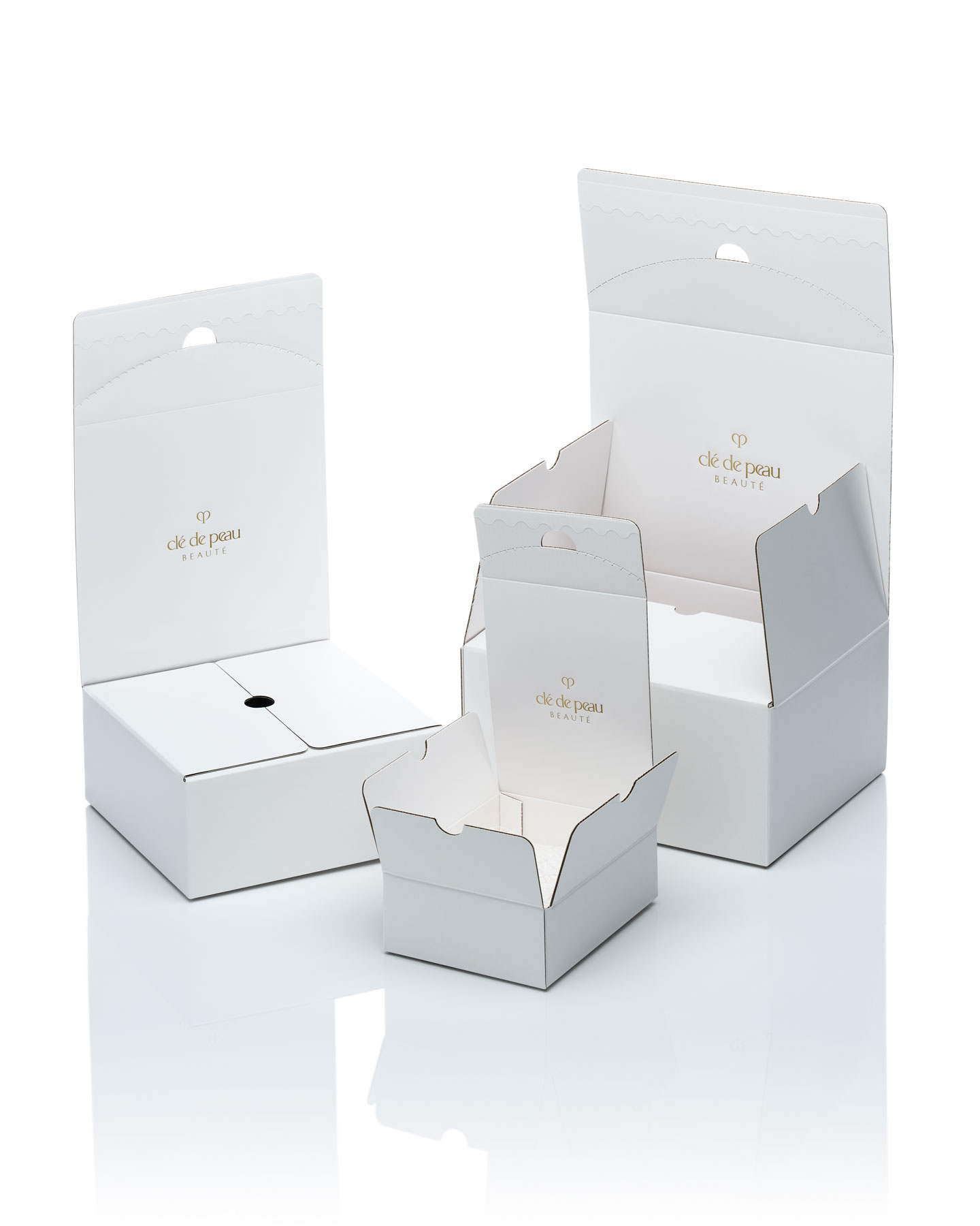 Photo of a white Clé de Peau Beauté shipping box, featuring the brand's logo in gold, shown in three stages to demonstrate the elegant design for a special unboxing experience.