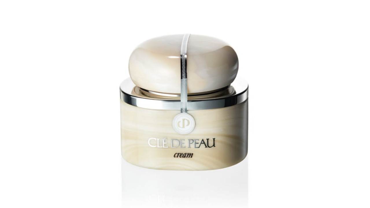 Photo of a beige container with a marble-like texture, featuring a rounded cap accented by a silver line. The front displays the brand logo and the product name “cream” (former packaging).