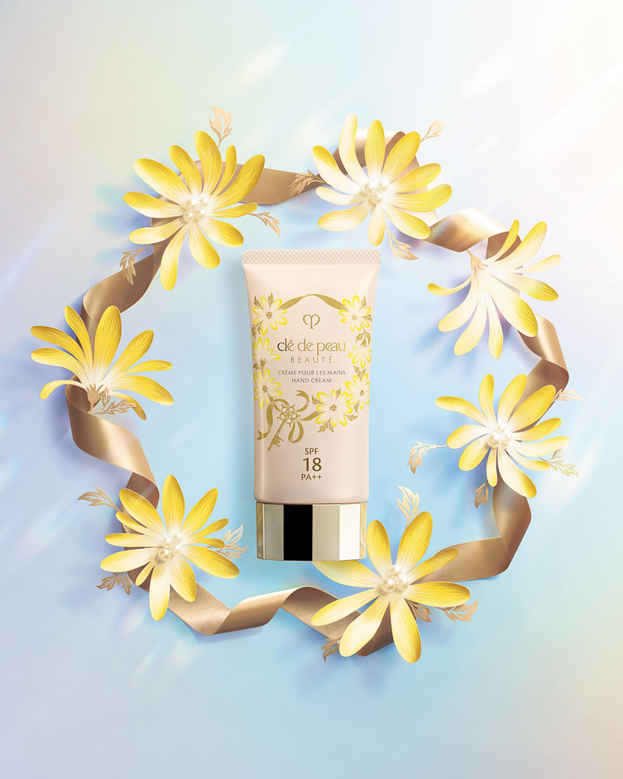 Photo of a HAND CREAM with a gold cap, surrounded by yellow flowers and a gold ribbon.