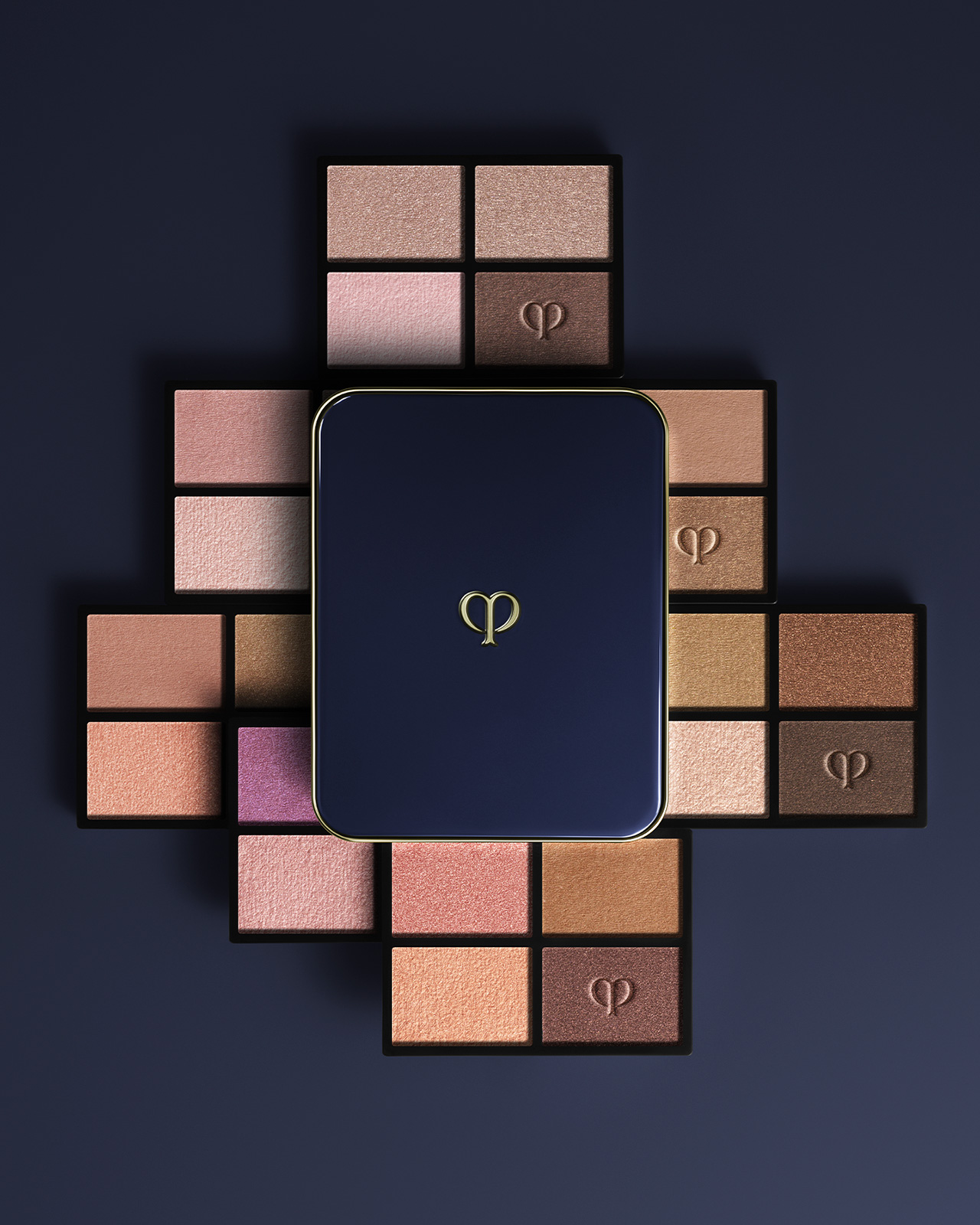 Photo of the EYE COLOR QUAD (REFILL) collection. A blue-black compact case is placed in the center, and refills in brown, pink, and bronze tones are arranged in a radial pattern.
