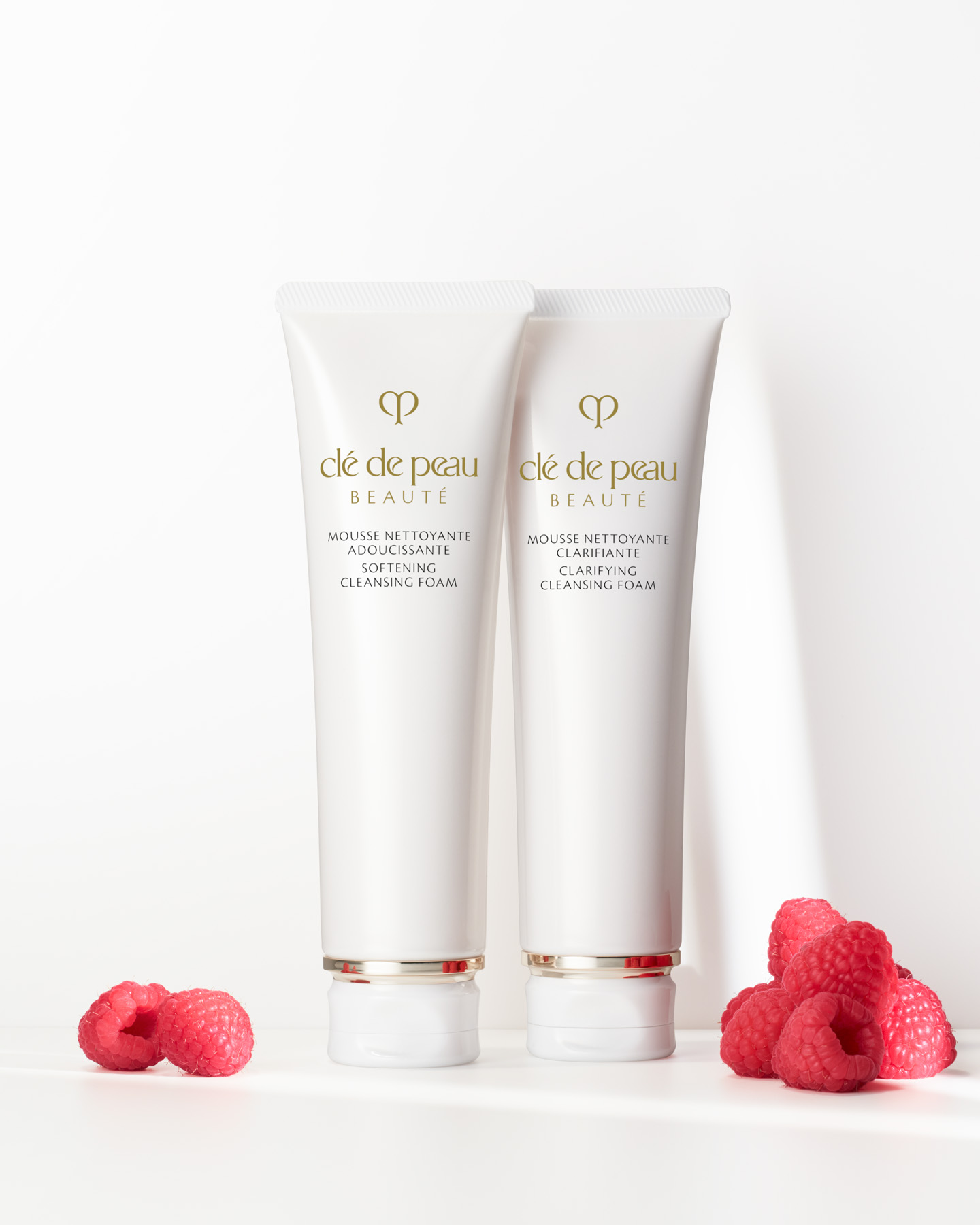 Photo of Clé de Peau Beauté SOFTENING CLEANSING FOAM and CLARIFYING CLEANSING FOAM tubes displayed with fresh raspberries, representing the raspberry extract used in both products.