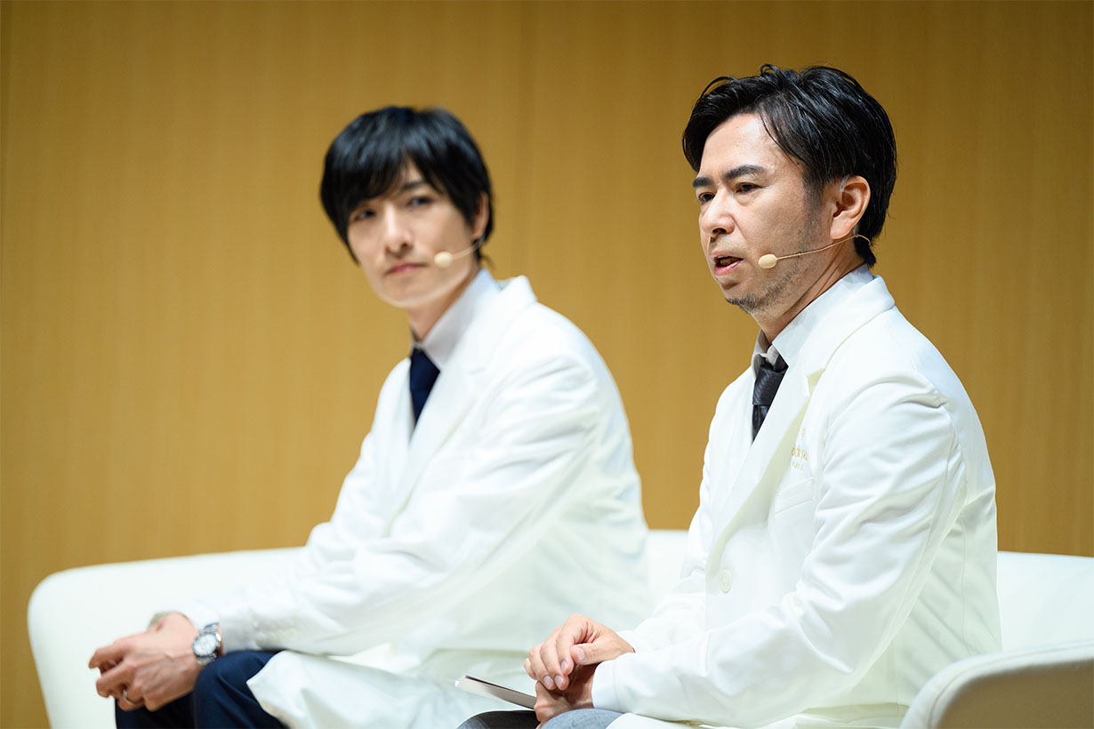 Photo of two men in white lab coats engaged in conversation. 