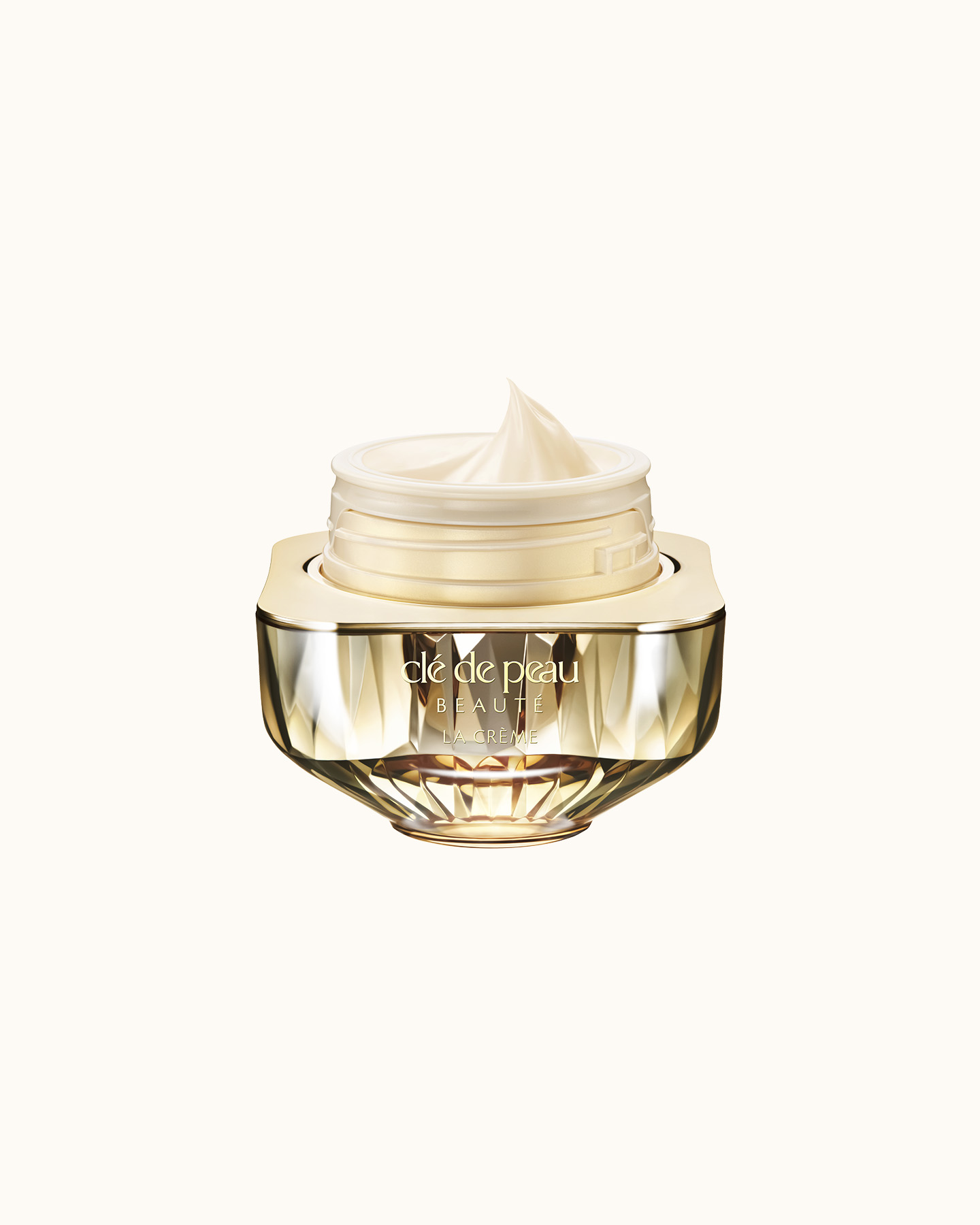 Photo of Clé de Peau Beauté’s high-performance cream “La Crème,” housed in a jewel-cut, translucent gold container. The lid is open, revealing the smooth cream inside.