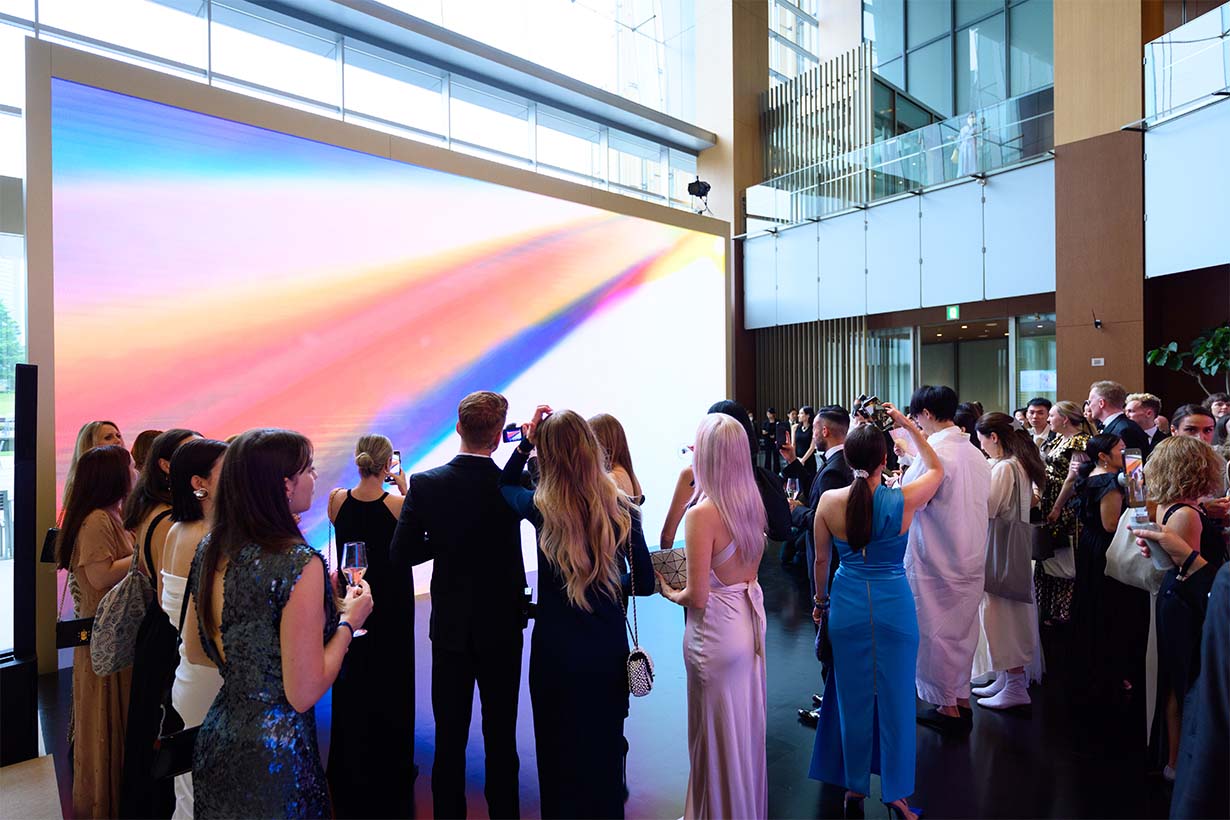 Photo of formally dressed individuals gathered in front of a digital artwork.