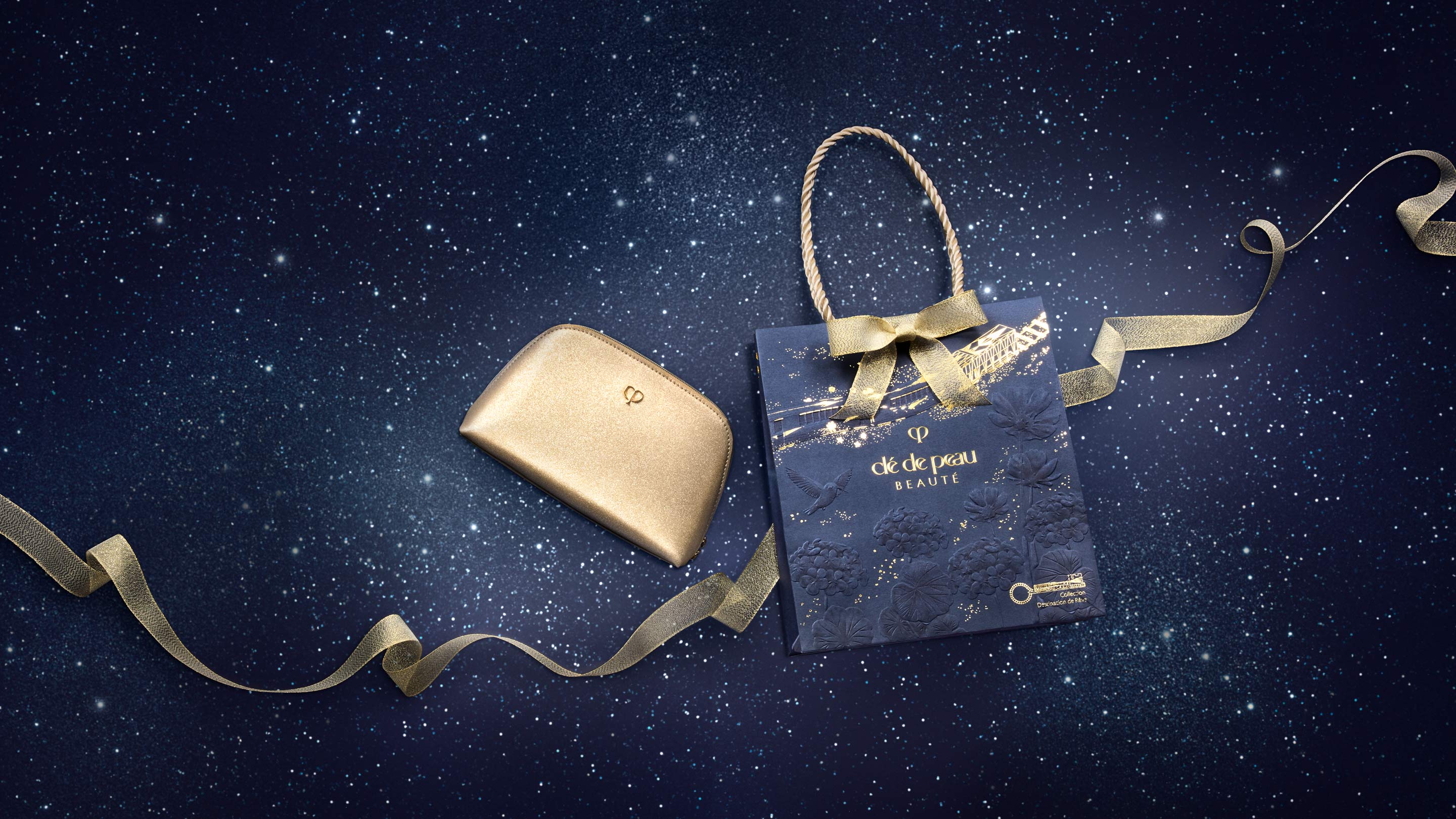 Photo of a luxurious Clé de Peau Beauté gift bag and a gold cosmetic pouch elegantly displayed with a flowing gold ribbon against a starry night sky, representing the 'Art of Gifting'.