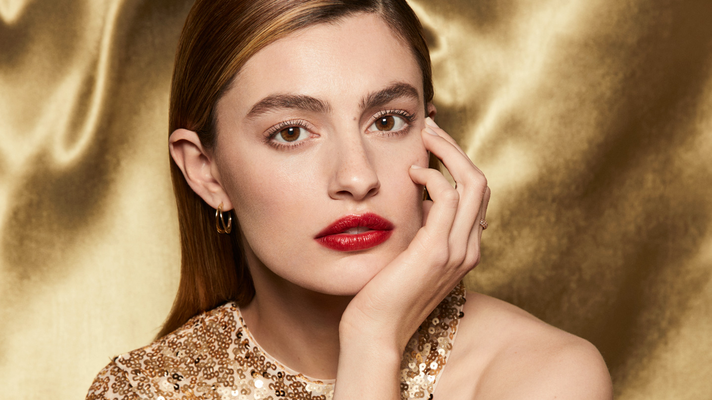 Photo of Clé de Peau Beauté ambassador wearing THE PRECIOUS LIPSTICK and posing gracefully in a gold dress.